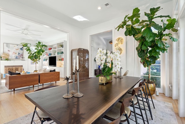 dining room featuring ceiling fan, a fireplace, and light hardwood / wood-style floors