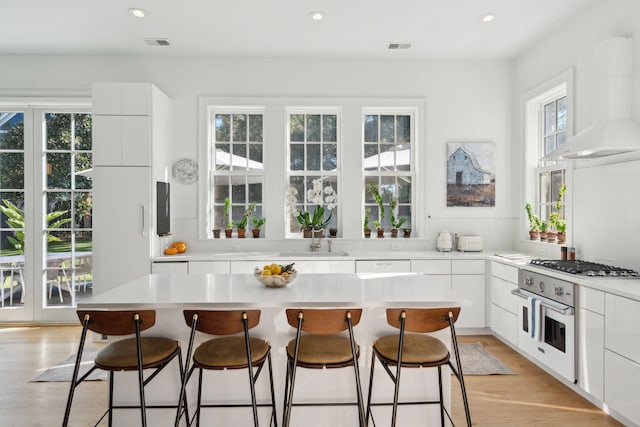 kitchen with white cabinets, white oven, extractor fan, and a healthy amount of sunlight