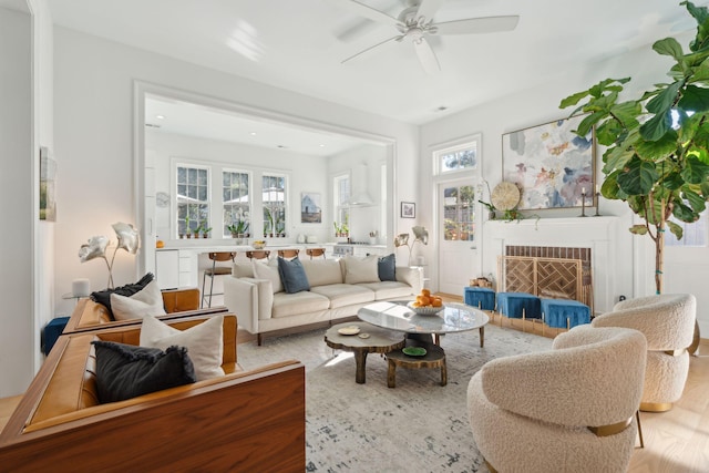 living room with a brick fireplace, ceiling fan, and light wood-type flooring