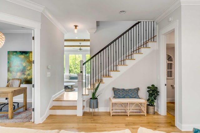 staircase with crown molding, a ceiling fan, baseboards, and wood finished floors