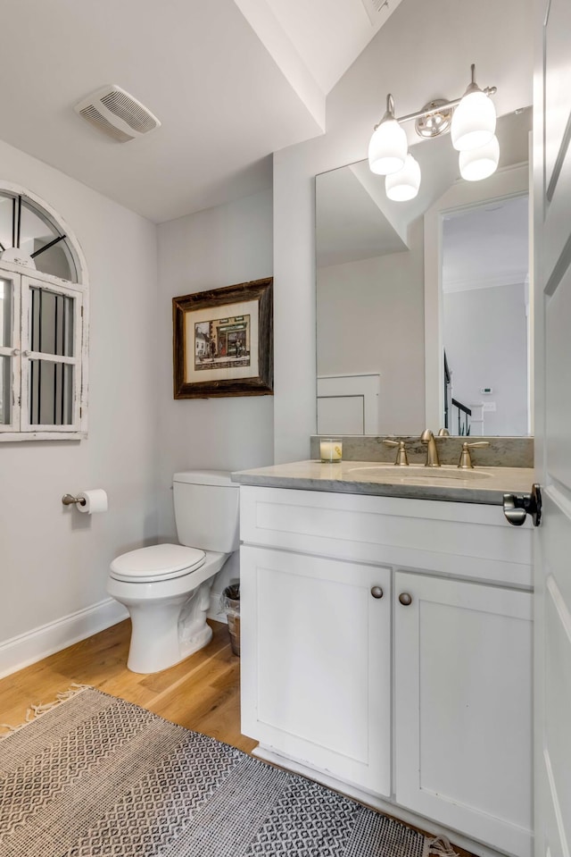 half bathroom featuring visible vents, vanity, wood finished floors, toilet, and baseboards