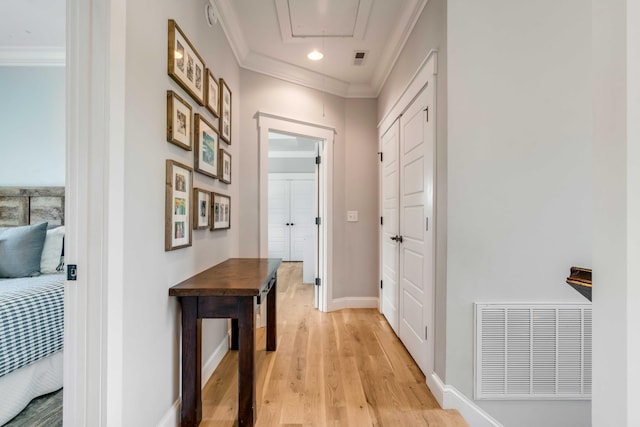 hall featuring attic access, visible vents, baseboards, ornamental molding, and light wood-style flooring