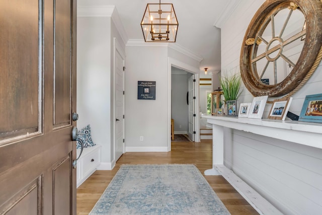 foyer entrance with ornamental molding, light wood-style flooring, and a notable chandelier