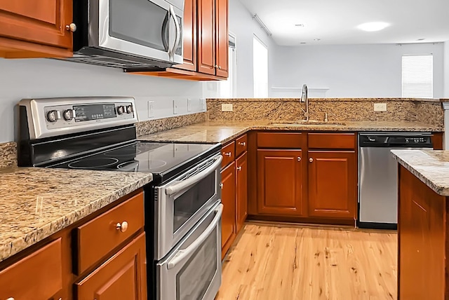 kitchen with stainless steel appliances, sink, light stone counters, light hardwood / wood-style flooring, and a healthy amount of sunlight