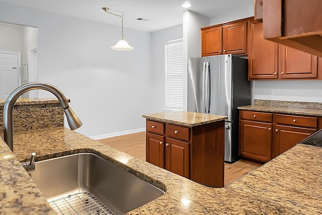 kitchen featuring pendant lighting, stainless steel fridge, sink, and light stone counters