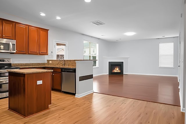 kitchen with sink, light hardwood / wood-style flooring, appliances with stainless steel finishes, light stone counters, and a kitchen island