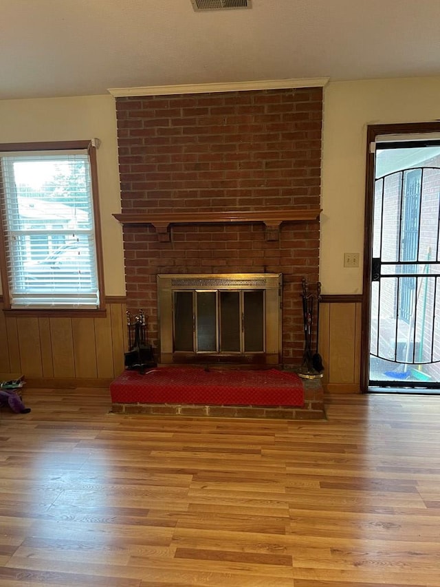 unfurnished living room with a brick fireplace, wooden walls, and light hardwood / wood-style flooring