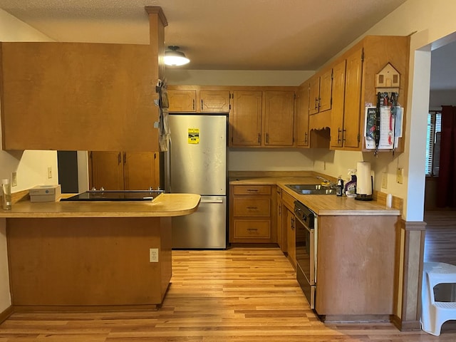 kitchen featuring black appliances, sink, light hardwood / wood-style floors, kitchen peninsula, and a textured ceiling