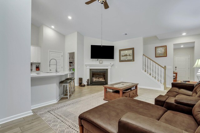 living room featuring a fireplace, light hardwood / wood-style flooring, ceiling fan, sink, and high vaulted ceiling