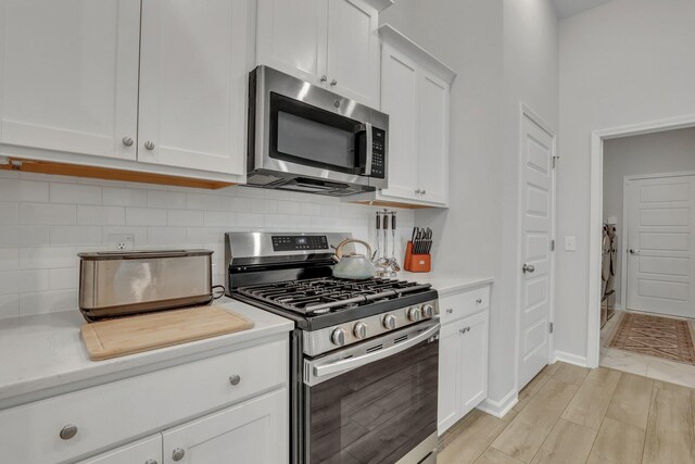 kitchen with white cabinetry, light hardwood / wood-style flooring, stainless steel appliances, and tasteful backsplash