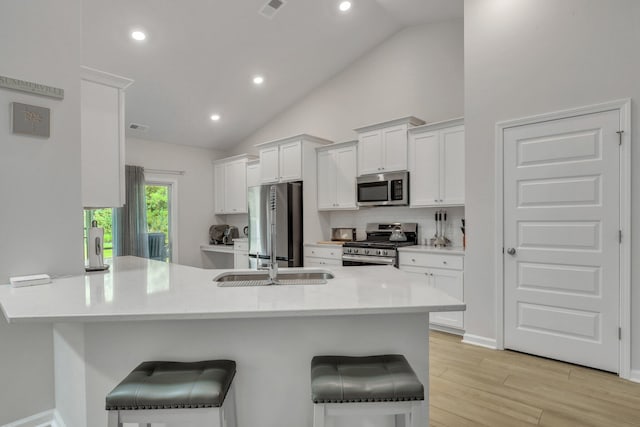 kitchen featuring light wood-type flooring, appliances with stainless steel finishes, white cabinetry, kitchen peninsula, and a kitchen bar