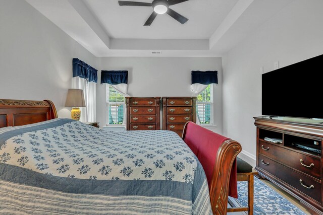 bedroom with a tray ceiling, ceiling fan, wood-type flooring, and multiple windows