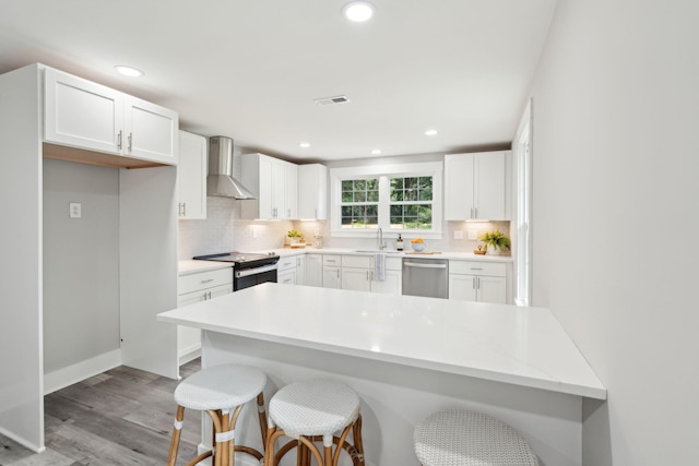 kitchen featuring a sink, a kitchen breakfast bar, white cabinets, dishwasher, and wall chimney exhaust hood