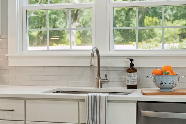 interior details with tasteful backsplash, light countertops, stainless steel dishwasher, and white cabinetry