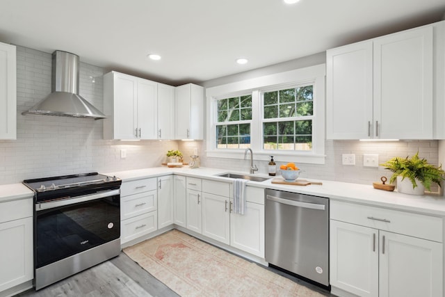 kitchen featuring wall chimney exhaust hood, appliances with stainless steel finishes, light countertops, and a sink