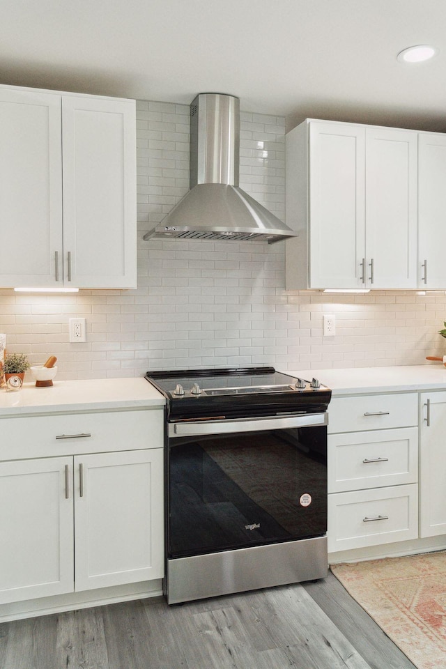 kitchen featuring wall chimney exhaust hood, light countertops, stainless steel range with electric stovetop, and white cabinets