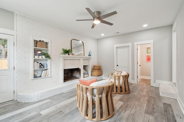 sitting room featuring ceiling fan, brick wall, a fireplace, baseboards, and light wood finished floors