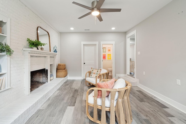 sitting room featuring light wood-type flooring, a brick fireplace, ceiling fan, and baseboards