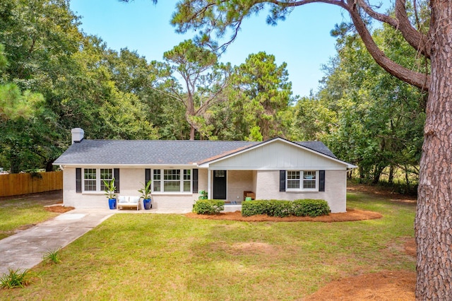 ranch-style house featuring a shingled roof, a chimney, fence, a front yard, and brick siding