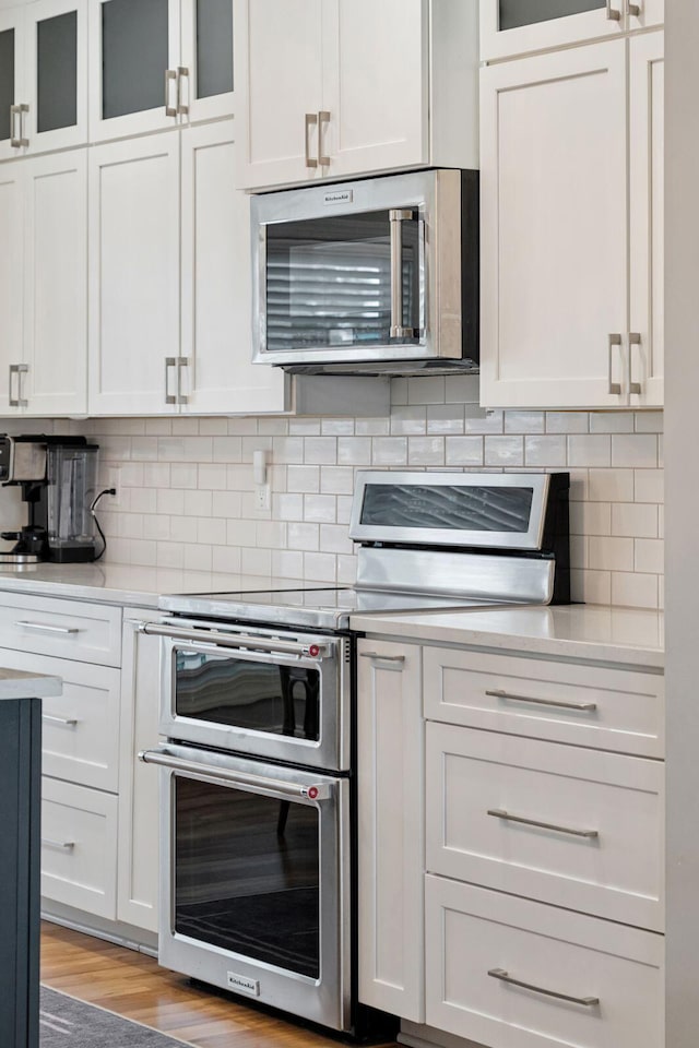 kitchen with tasteful backsplash, white cabinets, light countertops, light wood-type flooring, and stainless steel appliances