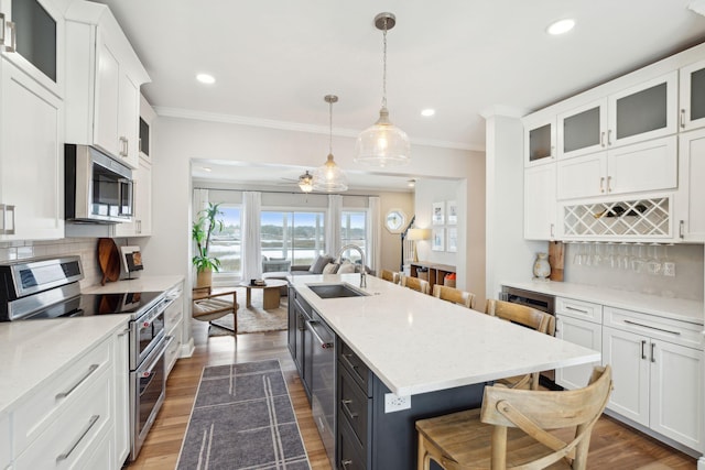 kitchen featuring crown molding, white cabinets, a kitchen bar, stainless steel appliances, and a sink