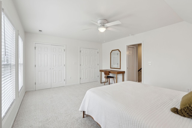 bedroom with light carpet, baseboards, two closets, and ceiling fan