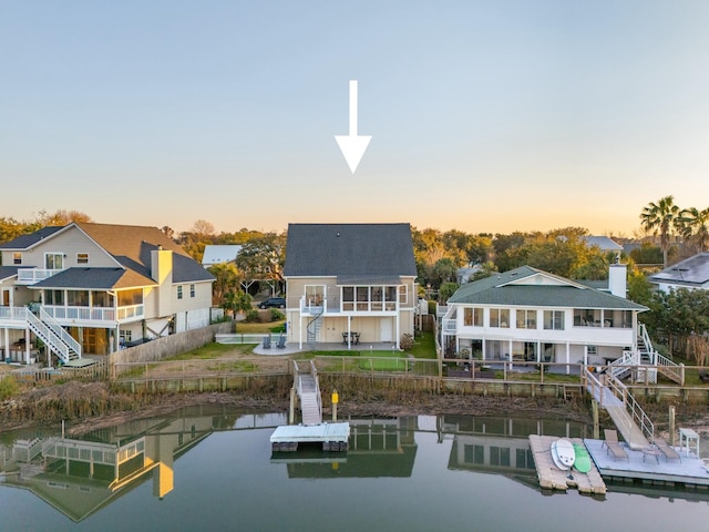 back of house at dusk with a water view, a residential view, stairway, and a shingled roof