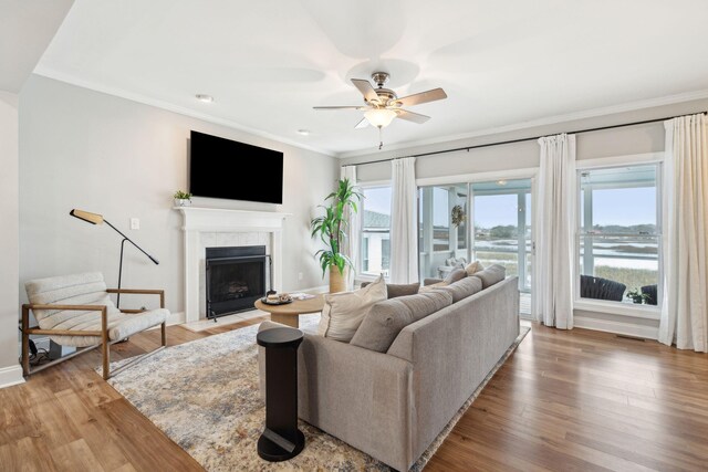 living area with a fireplace with flush hearth, light wood-type flooring, a ceiling fan, and ornamental molding
