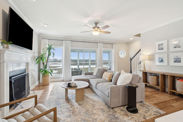 living area featuring ornamental molding, a fireplace, stairs, ceiling fan, and wood finished floors