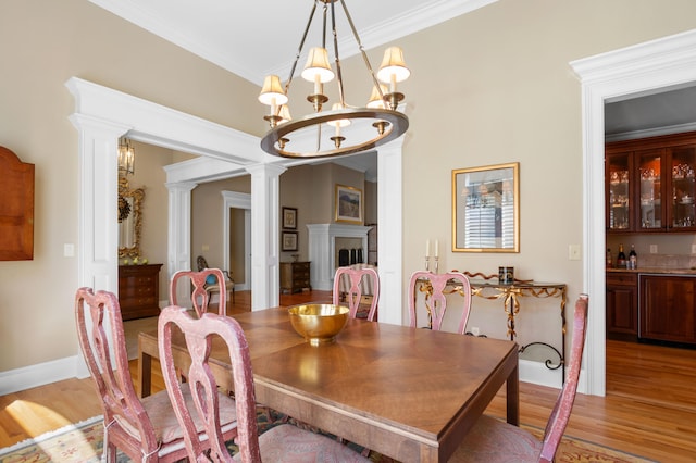 dining room featuring decorative columns, hardwood / wood-style flooring, crown molding, and a notable chandelier