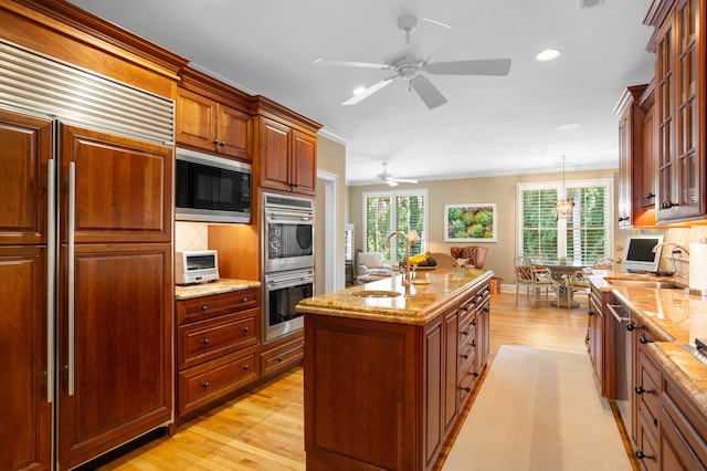 kitchen with a kitchen island with sink, built in appliances, sink, ceiling fan, and light hardwood / wood-style floors