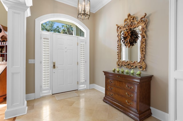 foyer entrance featuring crown molding, an inviting chandelier, and decorative columns