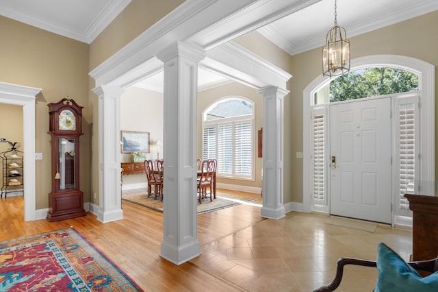 foyer entrance featuring light wood-type flooring, a healthy amount of sunlight, ornamental molding, and ornate columns