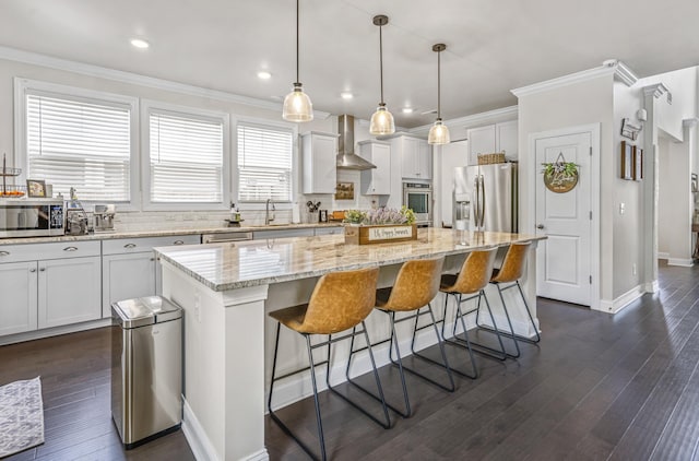 kitchen with pendant lighting, a center island, white cabinets, wall chimney range hood, and stainless steel appliances