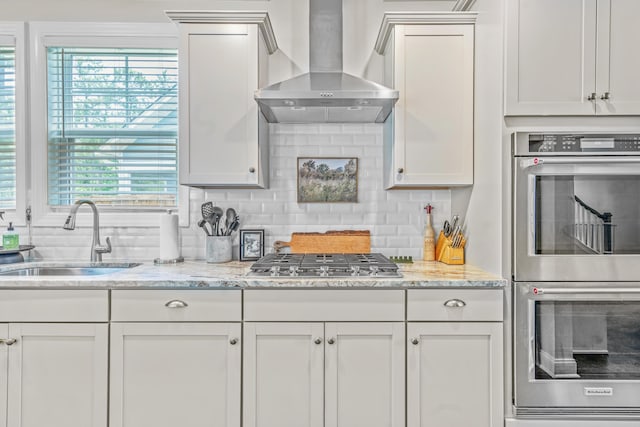 kitchen featuring backsplash, stainless steel appliances, sink, wall chimney range hood, and white cabinets