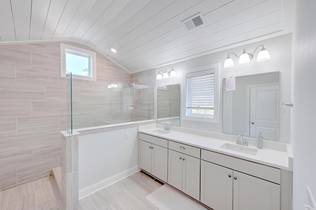 bathroom with vanity, a tile shower, lofted ceiling, and a healthy amount of sunlight