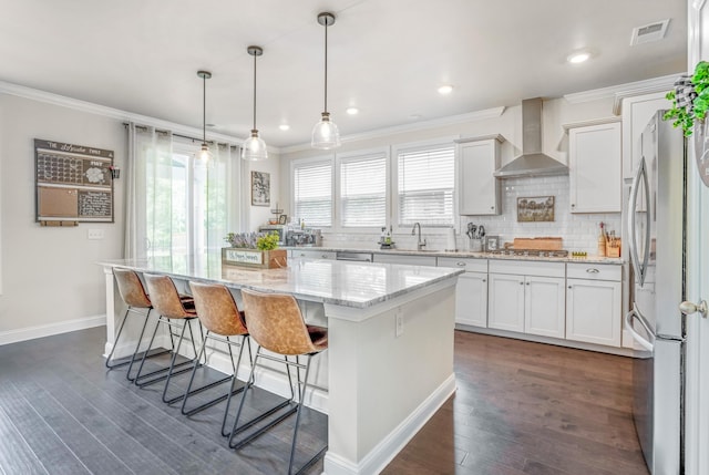 kitchen with a center island, white cabinets, wall chimney range hood, hanging light fixtures, and appliances with stainless steel finishes