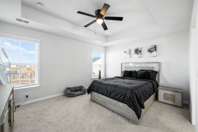 bedroom with multiple windows, light carpet, a raised ceiling, and ceiling fan