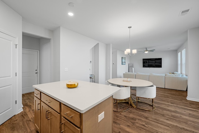 kitchen with ceiling fan, dark hardwood / wood-style flooring, a kitchen island, and pendant lighting