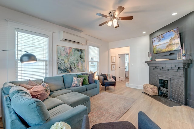 living room with a brick fireplace, light hardwood / wood-style flooring, ceiling fan, and a wall mounted air conditioner