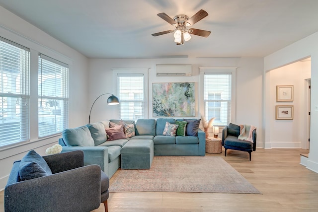 living room with a wall unit AC, ceiling fan, plenty of natural light, and light wood-type flooring