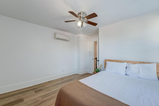 bedroom featuring ceiling fan, a wall mounted AC, and light hardwood / wood-style flooring