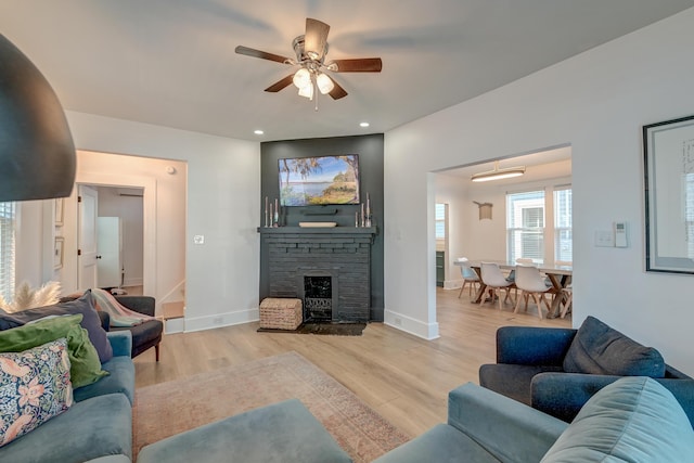 living room with a brick fireplace, ceiling fan, and light wood-type flooring