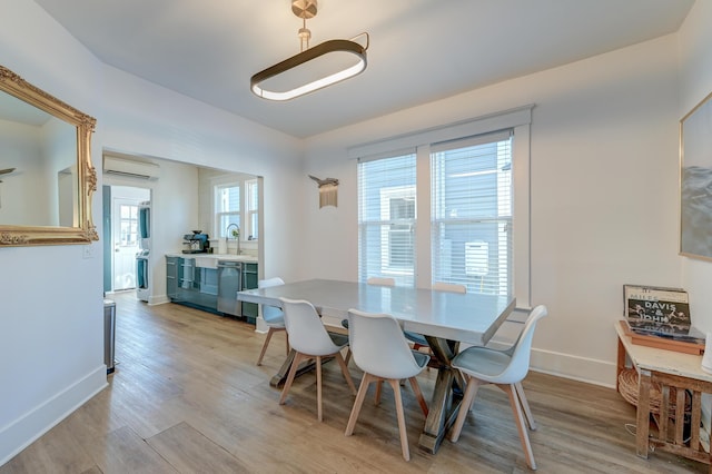 dining space featuring an AC wall unit, sink, and light hardwood / wood-style flooring