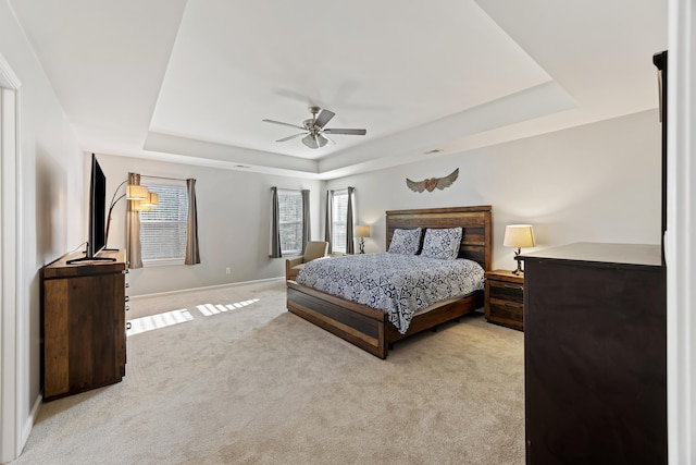 bedroom with ceiling fan, light carpet, visible vents, baseboards, and a tray ceiling