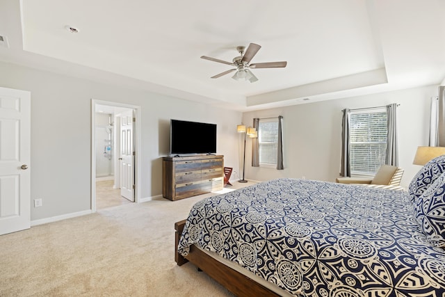 carpeted bedroom with a tray ceiling, visible vents, a ceiling fan, ensuite bath, and baseboards