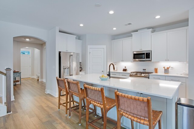 1607 Waterside Blvd, Moncks Corner, SC 29461 - kitchen featuring appliances with stainless steel finishes, a sink, light wood finished floors, decorative backsplash, and a kitchen island with sink
