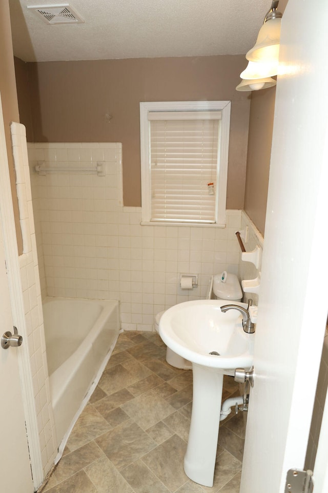 bathroom with tile walls, a washtub, and a textured ceiling