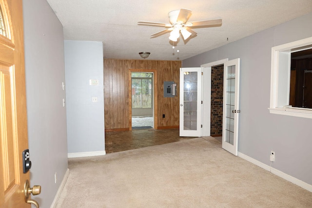 carpeted spare room featuring wood walls, ceiling fan, and a textured ceiling