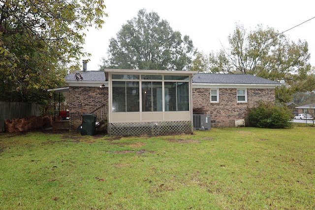 rear view of house with central AC unit, a sunroom, and a yard